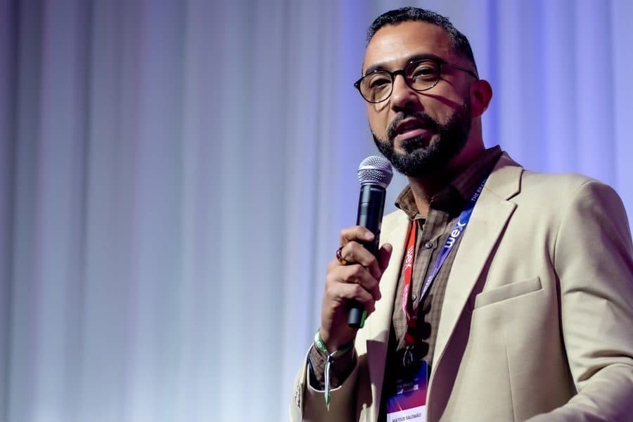 Mateus Salomão discursando em evento corporativo, crachá da WEX visível